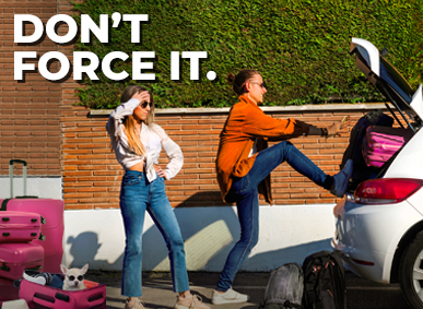 woman pushes luggage into the trunk of a small car while another woman stands watching with more luggage