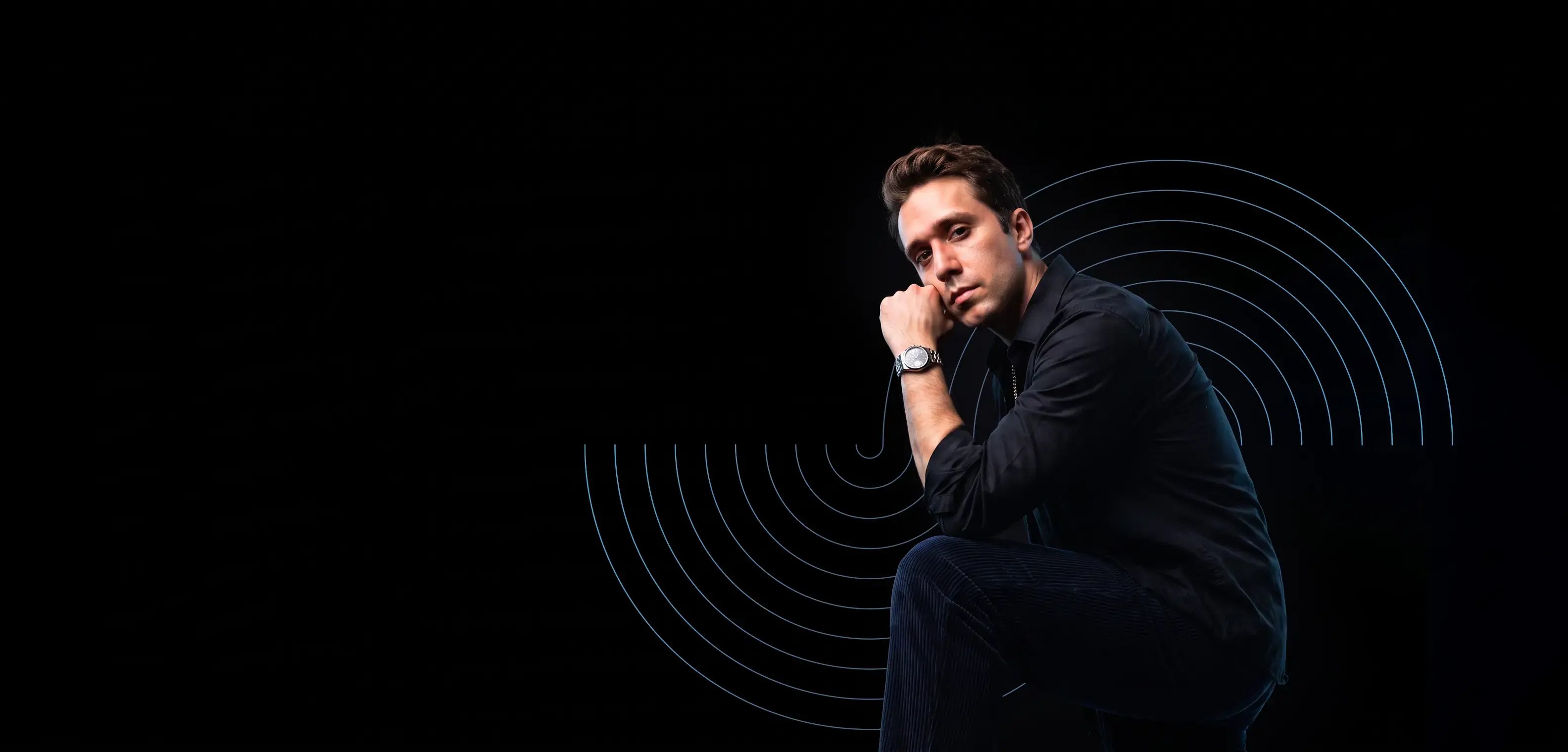 Young man standing with a dark overshirt against a black background with circular designs