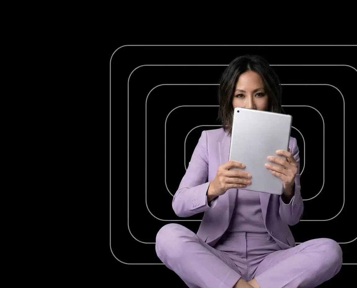 Woman wearing an all purple suit sitting holding a tablet that covers most of her face against a black background with geometric designs