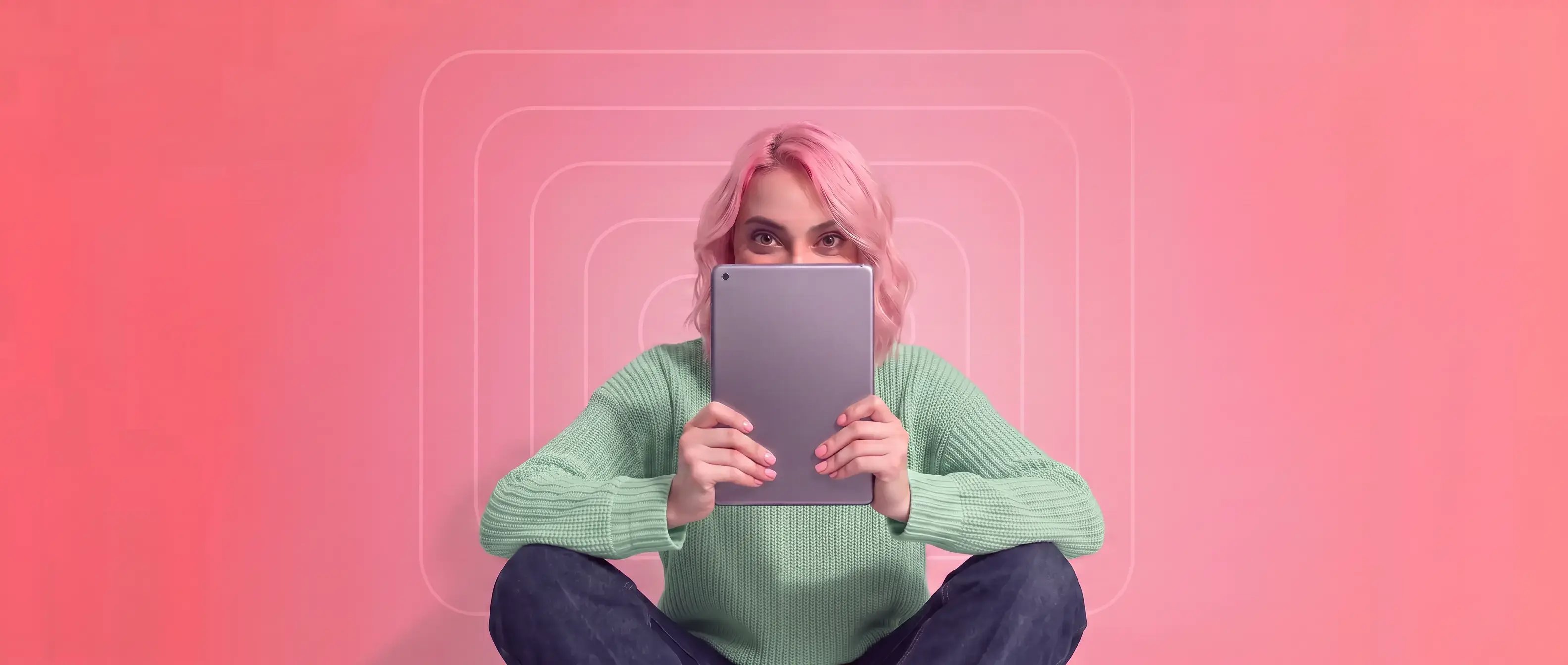 Woman with pink hair wearing a green sweater sitting on a pink background with geometric designs