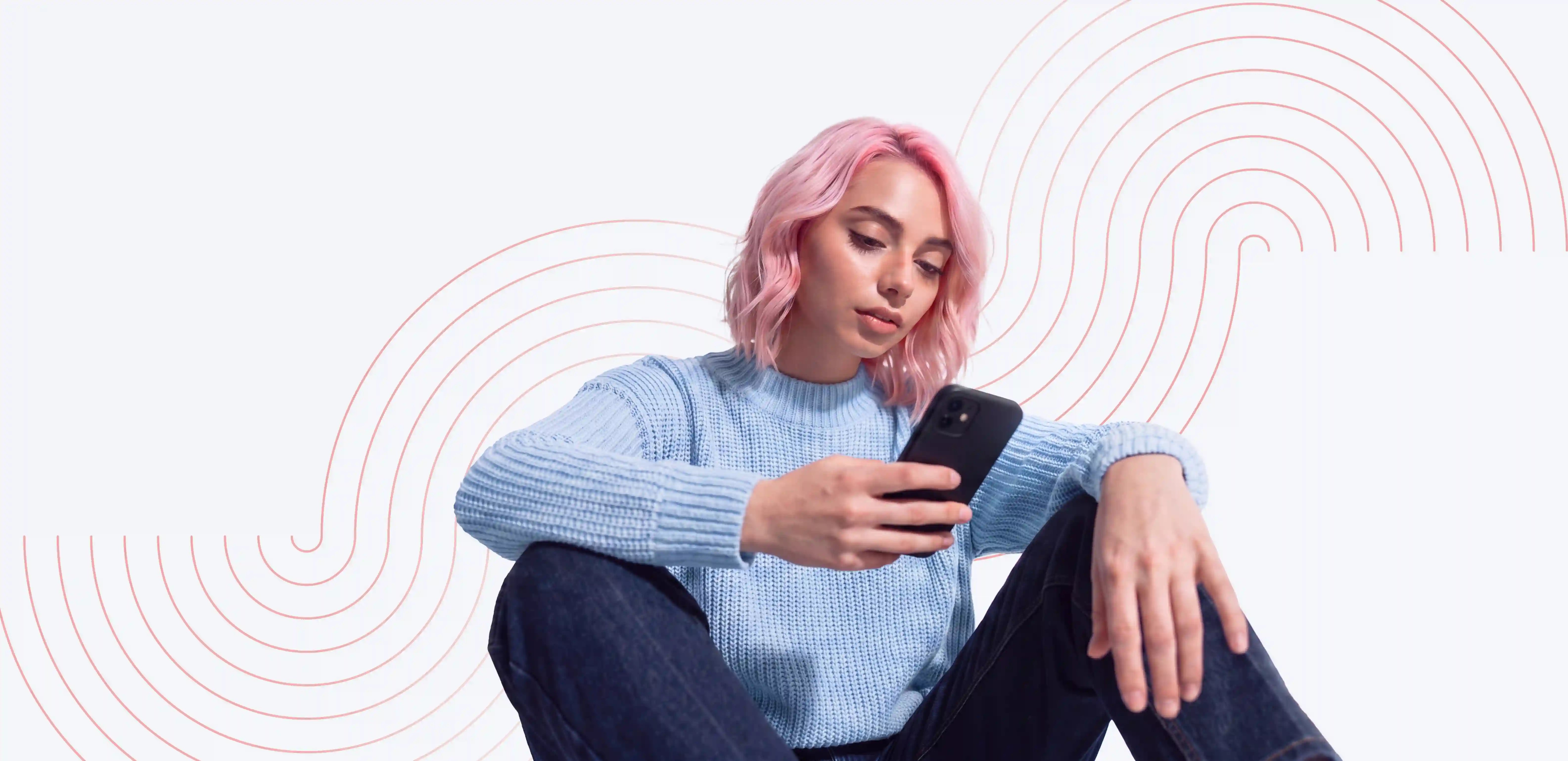 Woman with pink hair sitting and looking at her smartphone against a pale graphic background.